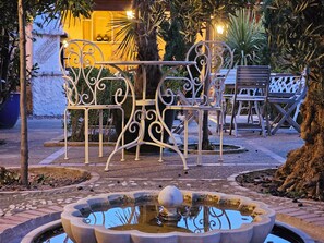 Une cour avec une fontaine, des chaises en métal et un banc.