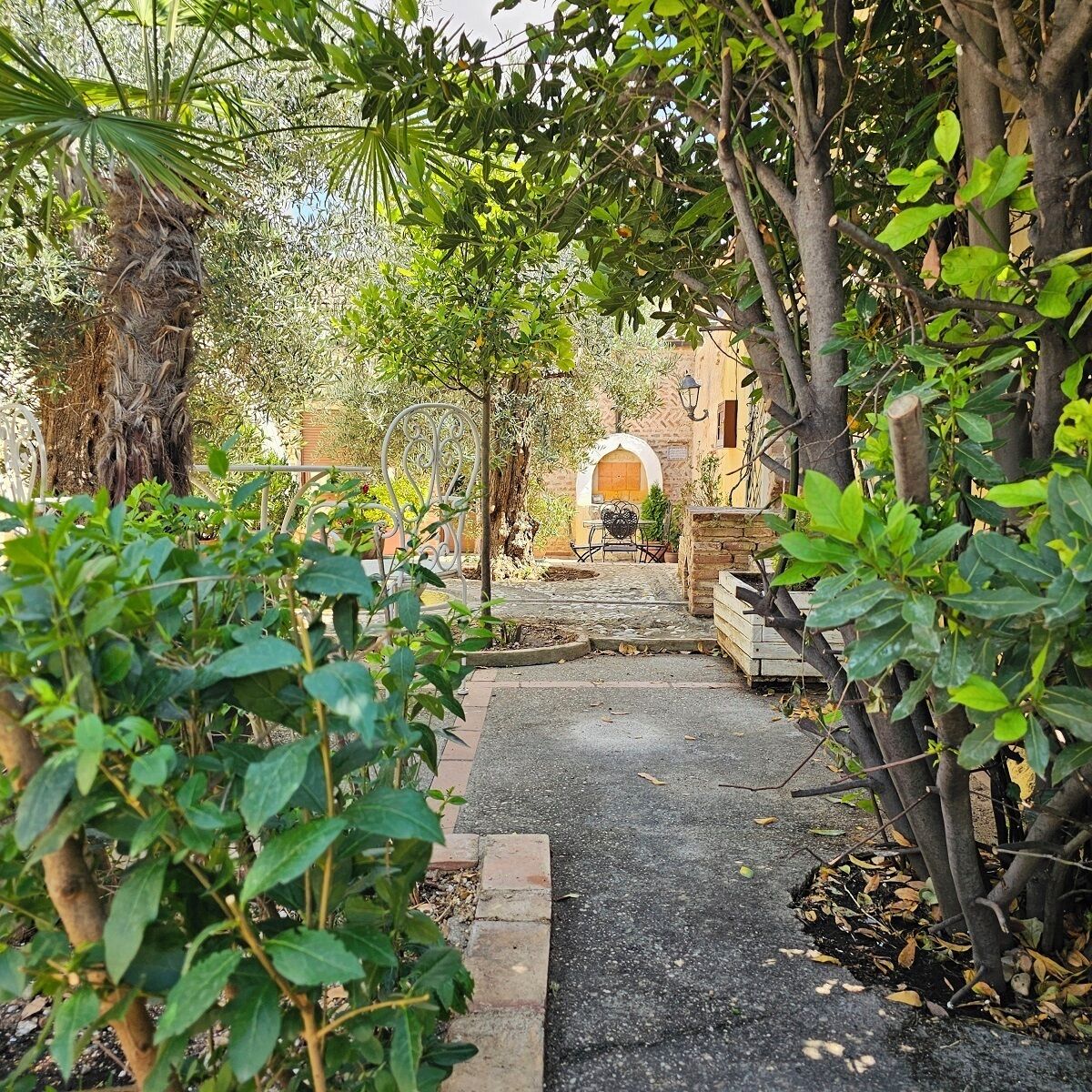 A pathway leading to a building with an arched entrance, surrounded by greenery and a small table with chairs.
