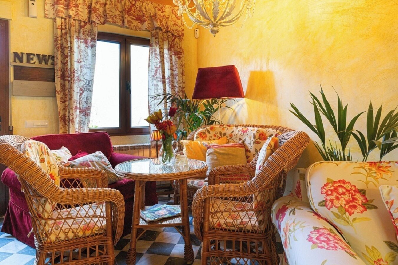 Una habitación con muebles de mimbre, un sofá floral, una mesa redonda y una ventana con cortinas.