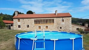 Ein Gebäude aus Stein mit rotem Ziegeldach und einem runden Swimmingpool mit blauer Abdeckung und Leiter.