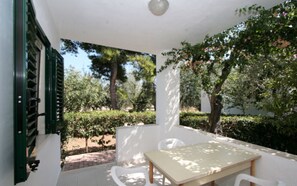 A covered patio with a table and chairs, surrounded by greenery and trees. - Three-room apartment in Residence - App 2 - with swimming pool near Vieste, Gargano, Puglia (Vieste)