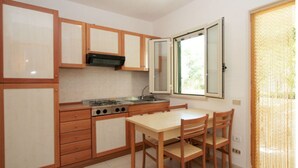 A compact kitchen with wooden cabinets, a gas stove, and a dining table with chairs. - Three-room apartment in Residence - App 2 - with swimming pool near Vieste, Gargano, Puglia (Vieste)
