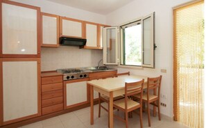 A compact kitchen with wooden cabinets, a gas stove, and a dining table with chairs. - Three-room apartment in Residence - App 2 - with swimming pool near Vieste, Gargano, Puglia (Vieste)