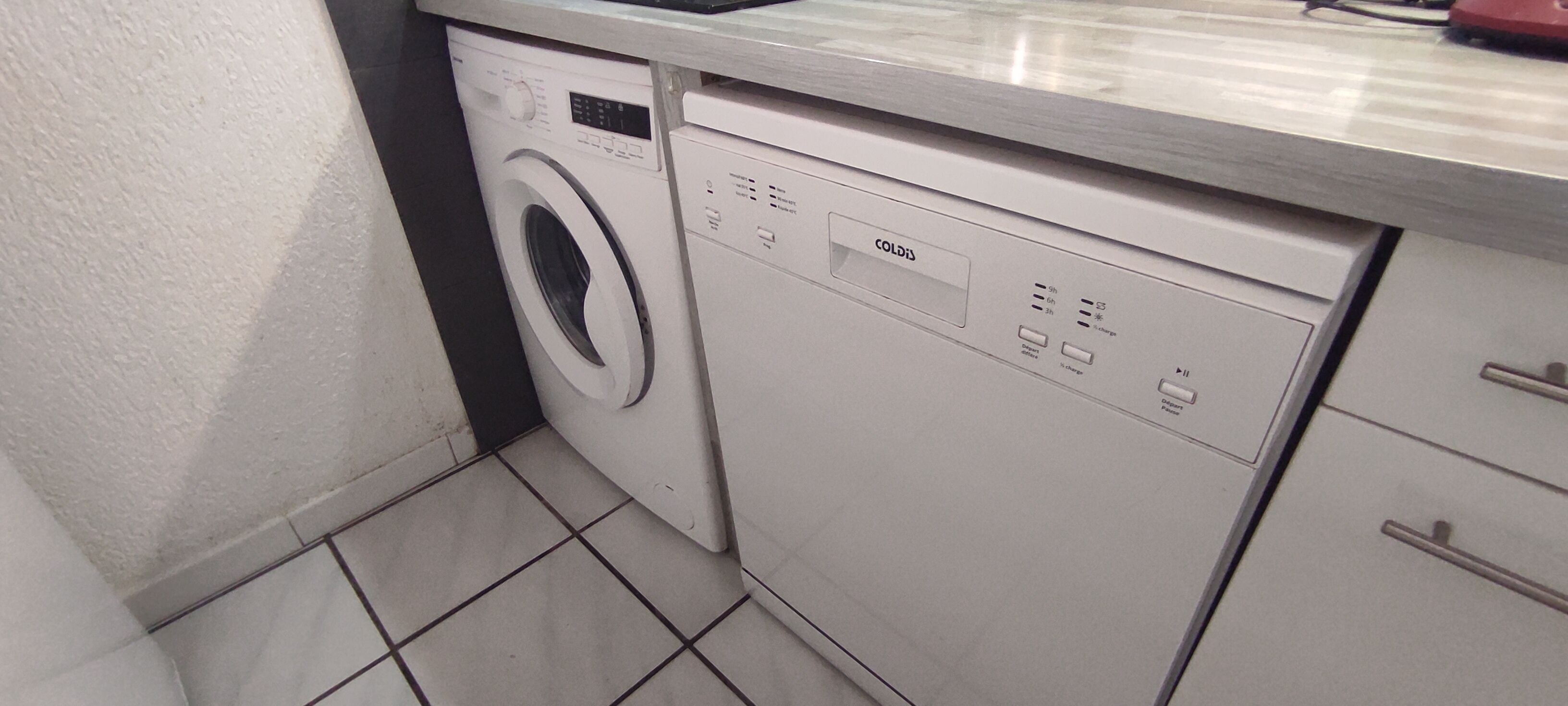 Una cocina compacta y moderna con lavadora y lavavajillas integrados, detalles en el salpicadero de azulejos y encimeras de acero inoxidable.