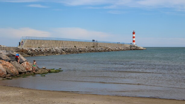 Un paysage côtier avec un phare, une côte rocheuse et une rambarde métallique bleue.