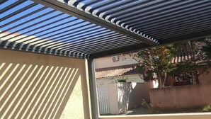 Une terrasse extérieure avec une table et des chaises, une pergola au-dessus et une vue sur un bâtiment en arrière-plan.