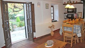 A dining area with a table set for four, a wooden bench, and a view of the garden through an open door.