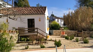 A white building with a tiled roof, a stone staircase, and a patio area with a pool and lounge chairs.