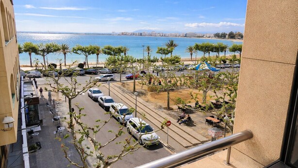 A view from a balcony overlooking a parking area with cars, a beach, and a cityscape in the distance. - P.C. LLEVANT 3 1 Roses (Rosas / Roses)