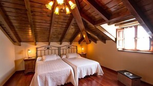 Ein Schlafzimmer mit zwei Betten, Holzboden, einer schrägen Decke mit freiliegenden Balken und einem Fenster mit Vorhängen.