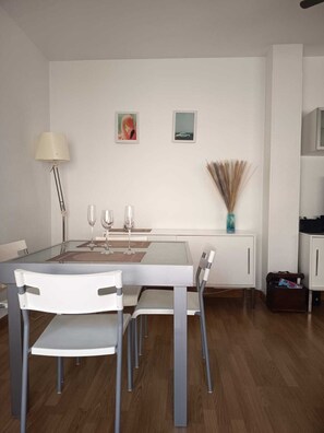 Un comedor moderno con una mesa de vidrio, sillas blancas, una lámpara y decoración en la pared.