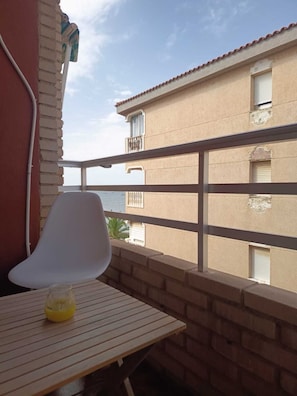 A balcony with a white chair and a glass table with a yellow object on it.