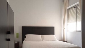 Un dormitorio con cama, ventilador de techo, ventana con cortinas y mesita de noche.