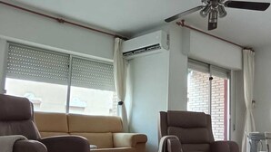 Una sala de estar con un sofá, dos sillones, un ventilador de techo y una ventana con persianas.