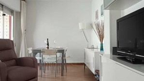 Una sala moderna con ventilador de techo, televisor de pantalla plana, comedor con mesa y sillas, y sofá.