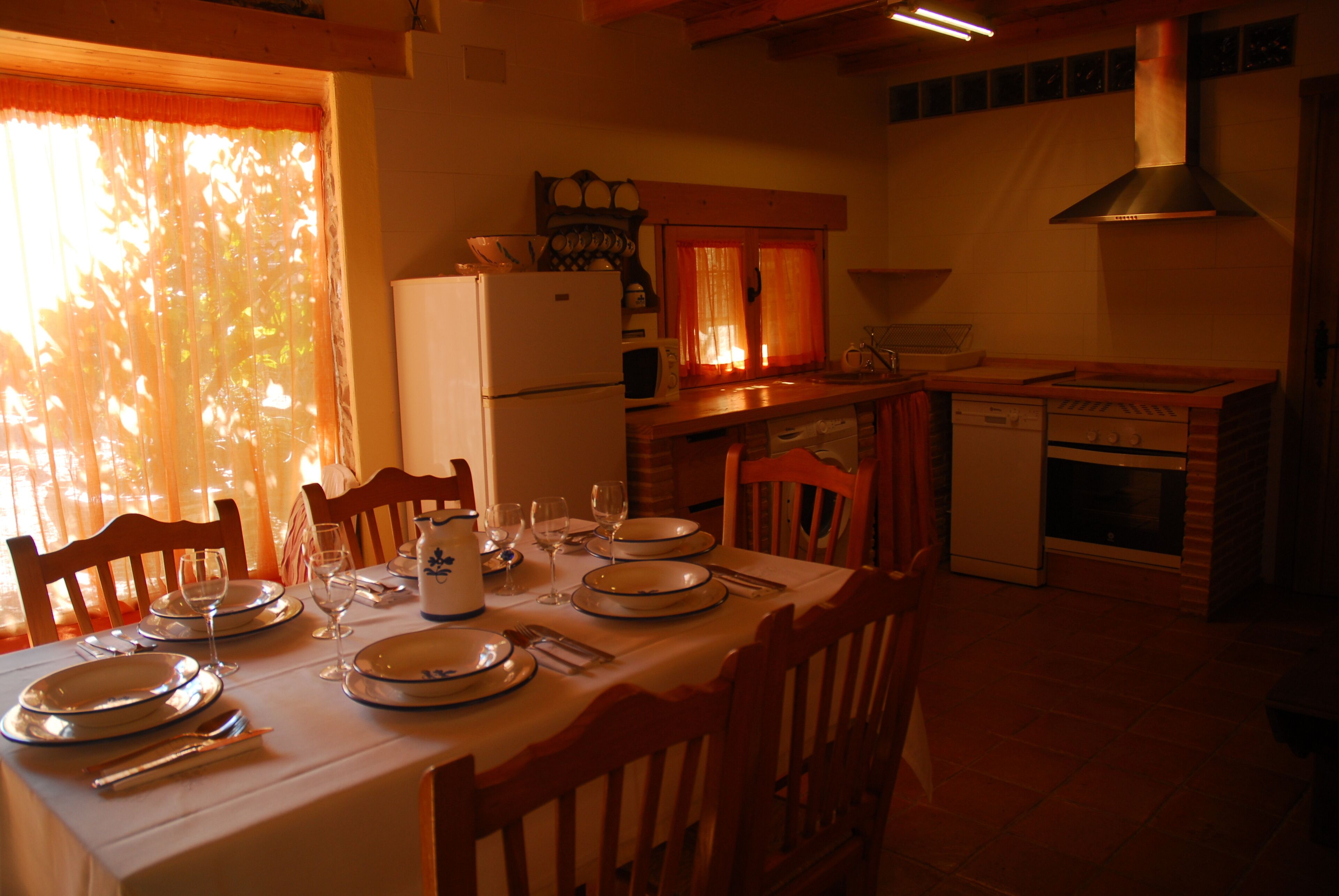 Comedor con una mesa preparada para cuatro personas, un refrigerador, un microondas y un lavamanos al fondo.
