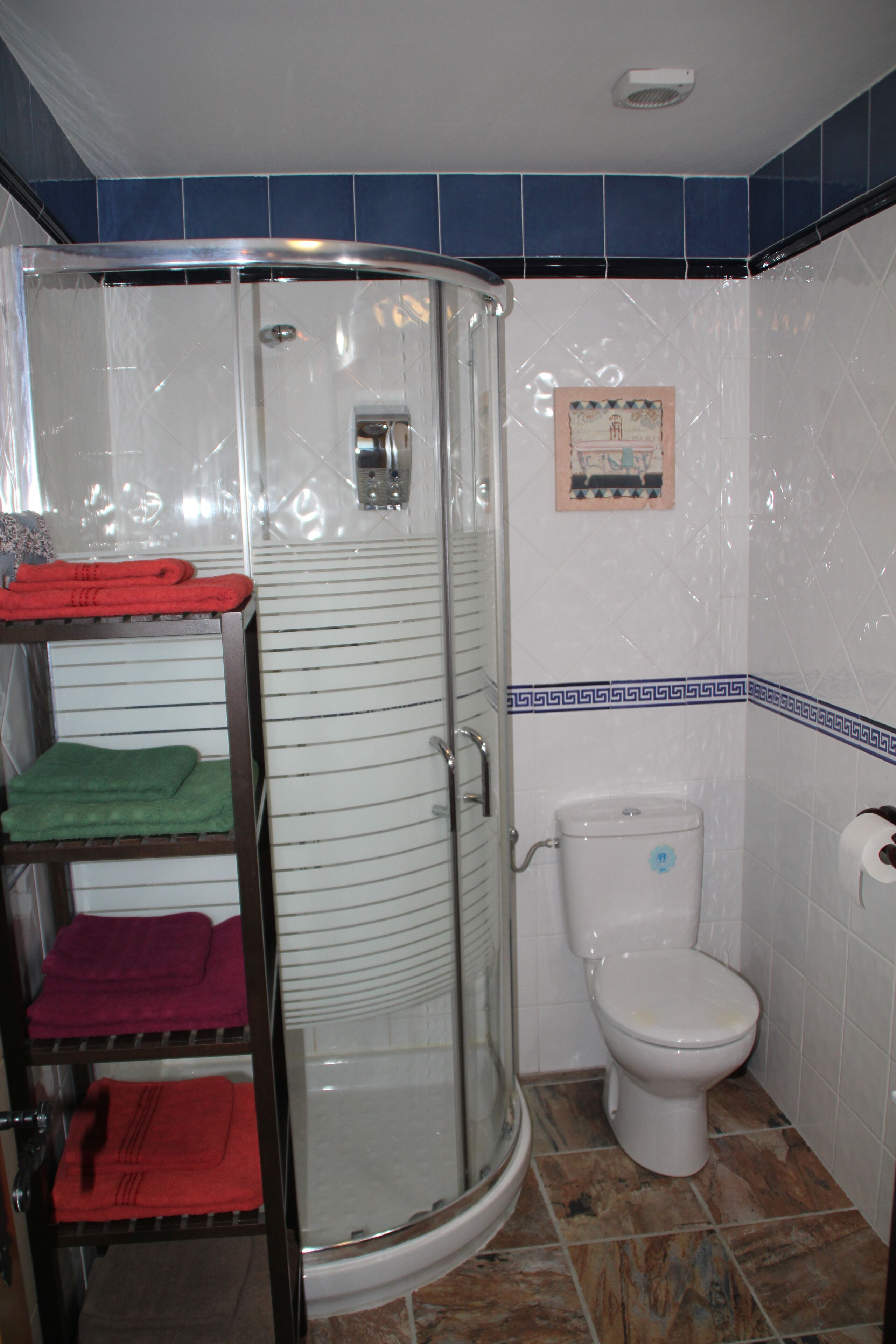 Un baño con ducha de vidrio, inodoro y un estante con toallas.