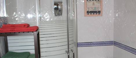 Un baño con ducha de vidrio, inodoro y un estante con toallas.