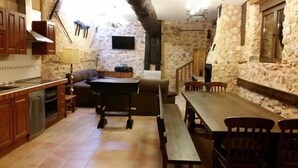 Una cocina rústica con paredes de piedra, muebles de madera y un comedor con banco y sillas.