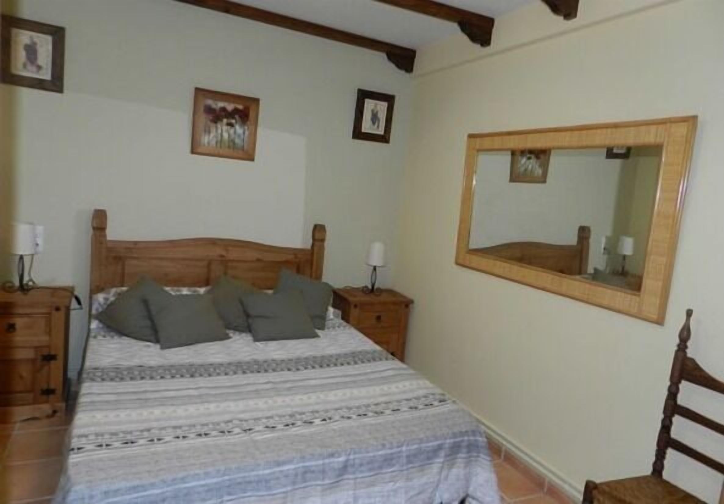 Un dormitorio con una cama de madera, dos mesitas de noche, un espejo y cuadros enmarcados en la pared.