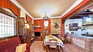 Un salon chaleureux avec un canapé rouge, une table basse en bois et un coin repas avec une table dressée pour quatre personnes.