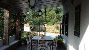 Un patio couvert avec une table et des chaises, des murs en pierre et une vue sur une piscine et la verdure.