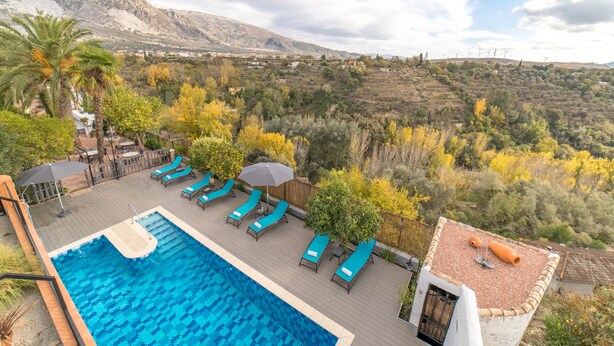 A swimming pool with lounge chairs and umbrellas, surrounded by trees and mountains in the background. - Alojamiento Rural El Valle for 6 people (Dúrcal)