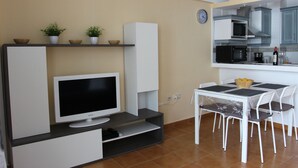 A compact kitchen with a microwave, stove, and dining area with a table and chairs. - Apartment right on the beach of Playa de La Arena, with balcony and sea view (Santiago del Teide)