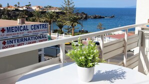 A balcony with a potted plant, overlooking a coastal area with a medical center sign in the background. - Apartment right on the beach of Playa de La Arena, with balcony and sea view (Santiago del Teide)