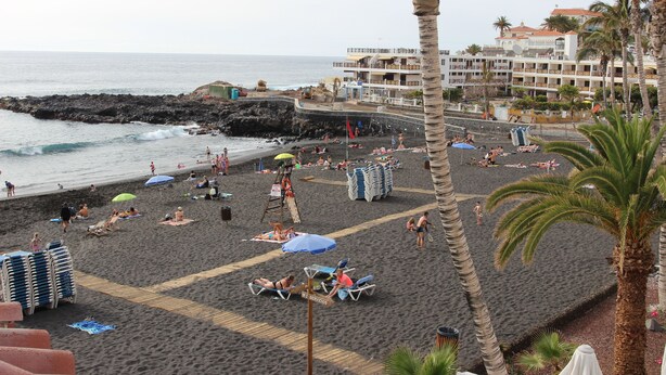 A beach with sun loungers, umbrellas, and a lifeguard stand. - Apartment right on the beach of Playa de La Arena, with balcony and sea view (Santiago del Teide)