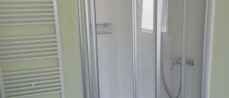 A shower enclosure with a glass door, a towel rack, and a wooden stool.