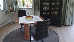 Un comedor con una mesa redonda, sillas tapizadas grises, un tapete gris y un mueble negro con puertas de vidrio.