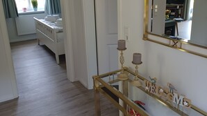 Un pasillo con un radiador blanco, una cuna blanca y una mesa consola de cristal con un cartel que dice 'WELCOME'.