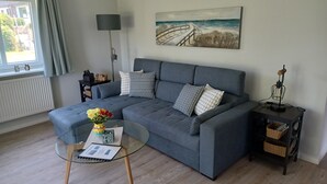 Una sala de estar moderna con un sofá gris, una mesa de centro de vidrio y un cuadro de una escena costera.