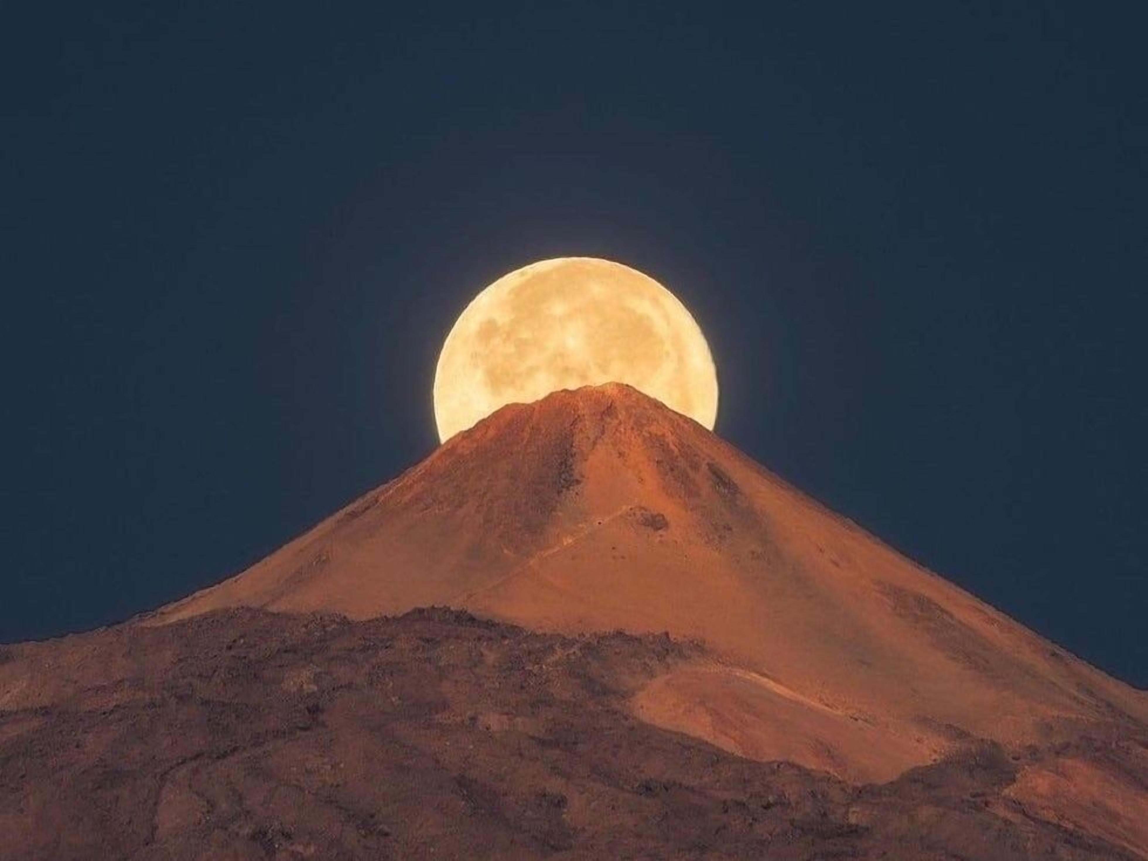 A mountain with a large full moon in the background.