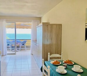 Una habitación con balcón, una mesa de comedor dispuesta con platos y tazas, y vista al mar.