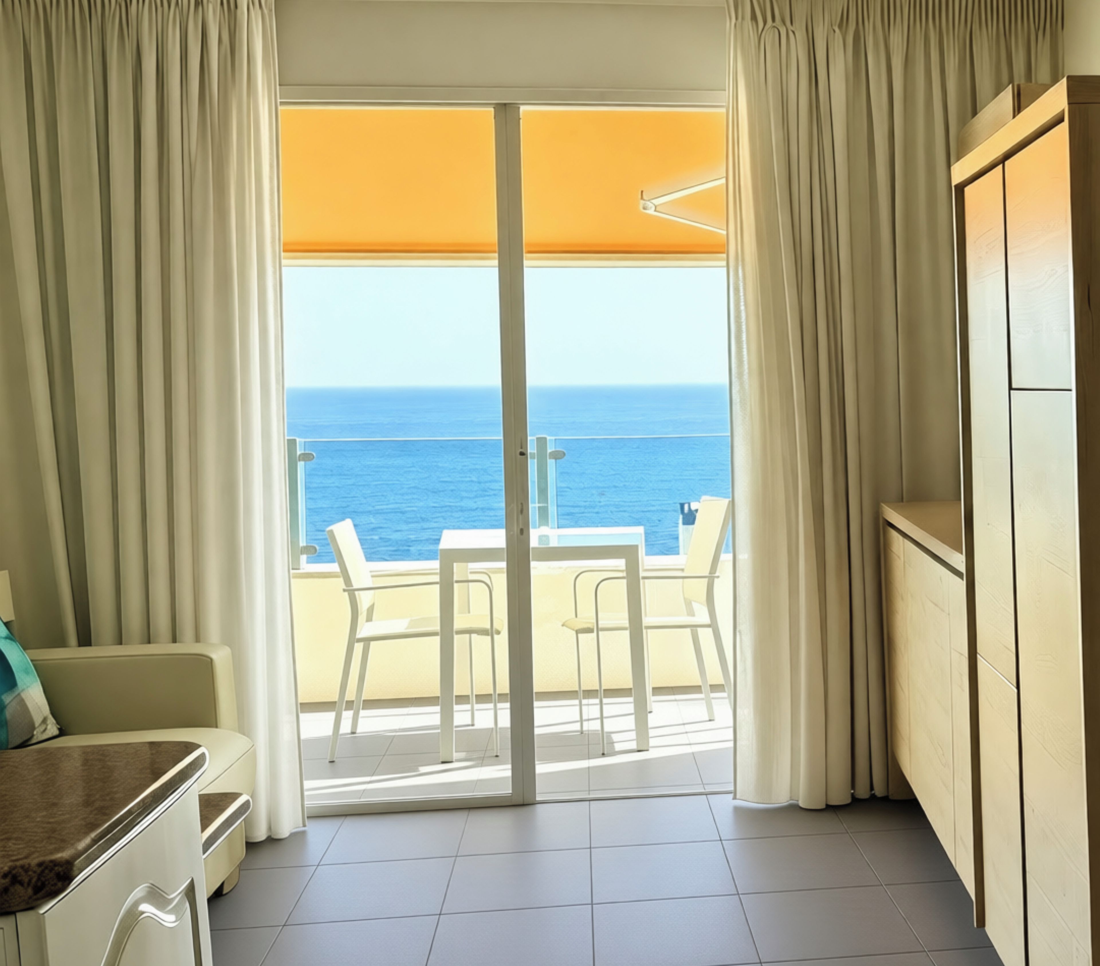 A room with a view of the ocean, a sliding glass door, a table with chairs, and a wooden cabinet.