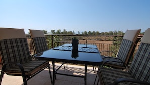 A balcony with a table and four chairs, a potted plant on the table, and a view of trees and a fence in the background. - First floor independent apartment with amazing views & private pool in Pessada (Livathos)