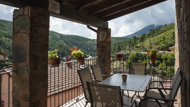 A covered outdoor seating area with stone pillars, a table, and chairs, overlooking a mountainous landscape with potted plants. - Rural apartment Ramajal Rural for 4 people (Pinofranqueado)