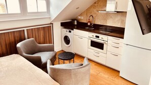 A compact kitchen with a washing machine, oven, and a refrigerator. There is a small dining area with a table and chairs. - Stunning Kensington Studio, Central London (London)