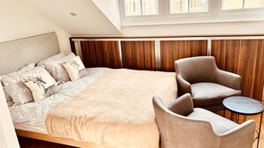 A bedroom with a large bed, a chair, a small table, and a window with a view of buildings. - Stunning Kensington Studio, Central London (London)