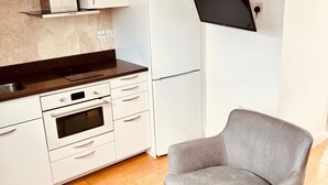A compact kitchen with white cabinets, a black countertop, and a built-in oven. There is a grey sofa and a small black table in the living area. - Stunning Kensington Studio, Central London (London)