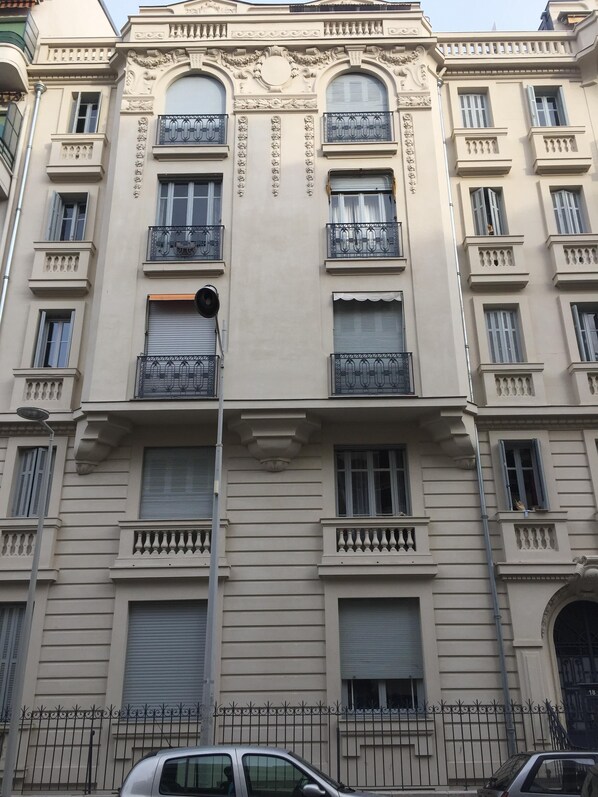 A multi-story building with balconies, large windows, and a metal fence in front.