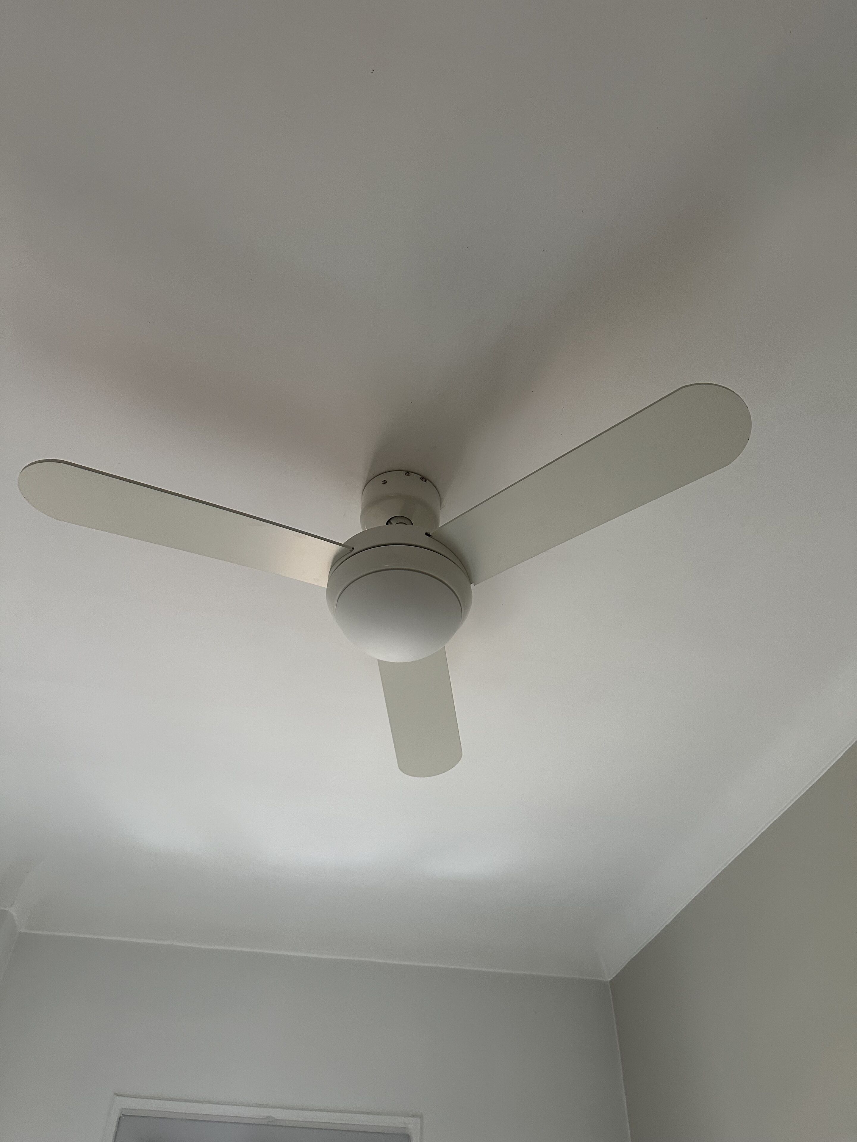 A ceiling fan with three blades in a room with white walls and a door.