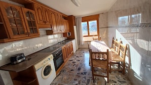 A kitchen with wooden cabinets, a washing machine, a dining table with chairs, and a view through a window. - Sol apartment ideal for large families and to visit the Monasterio de Piedra. (Munébrega)