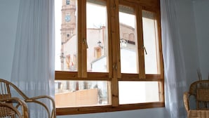 A room with a large window, wicker chairs, and a view of a clock tower. - Sol apartment ideal for large families and to visit the Monasterio de Piedra. (Munébrega)