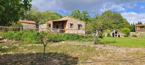 A stone house with a tiled roof, surrounded by greenery and a fenced yard.