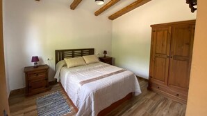A bedroom with a bed, wooden headboard, nightstands, a lamp, a wardrobe, and a wooden ceiling.