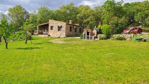 A stone house with a covered porch, a small garden, and a red car parked nearby.