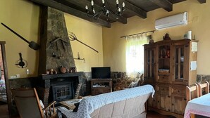 A cozy living room with a stone fireplace, a television, a wooden cabinet, and a dining area.